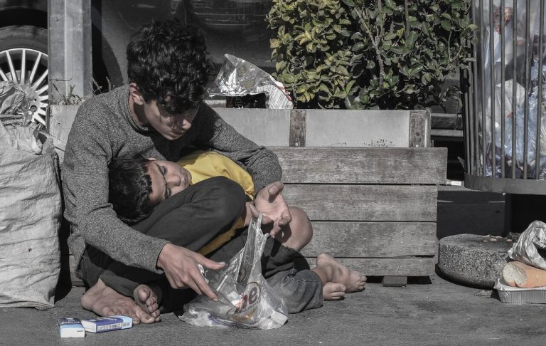Homeless kid with his brother sitting on the street desperately