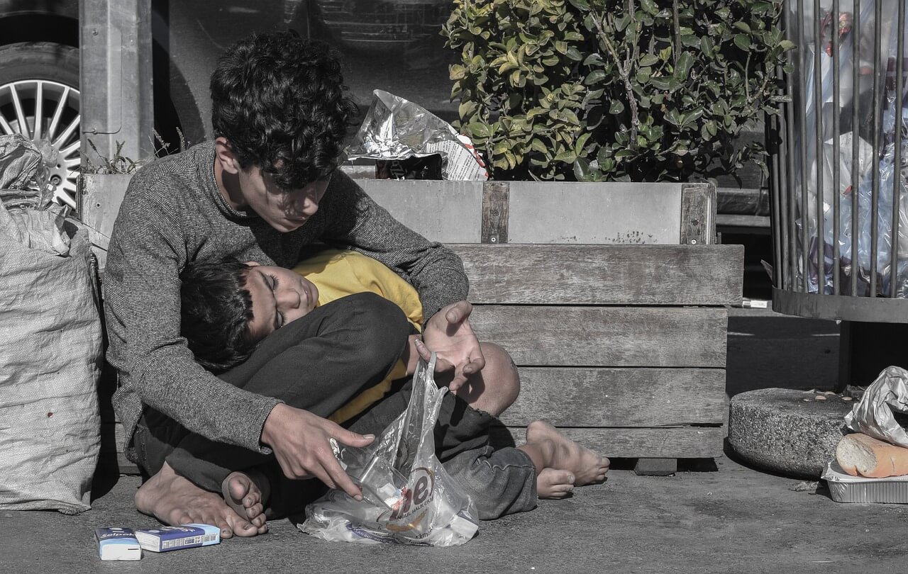Homeless kid with his brother sitting on the street desperately