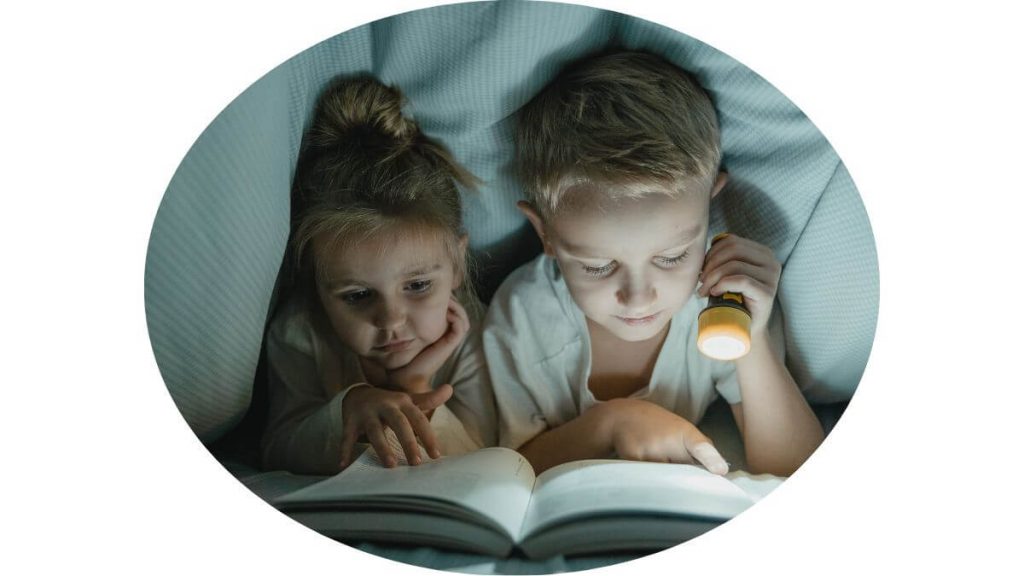 siblings reading under blanket with a flashlight